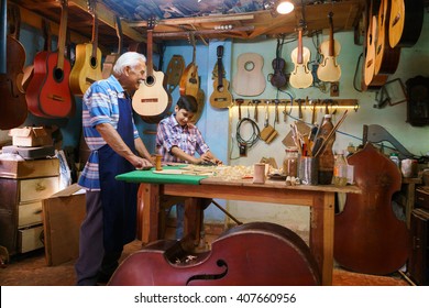 Small family business and traditions: old grandpa with grandson in lute maker shop. The senior artisan teaches to the boy how to chisel wood to make a music instrument