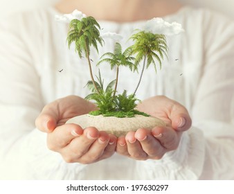 Small fantastic island with  palms in women's hands. Tropical vacation