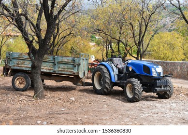 small farm tractor with cargo trailer in olive garden in finish agriculture season in autumn