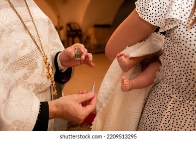 Small Feet Of A Child In A Dark Orthodox Church During The Sacrament Of Baptism. The Priest Is Next To The Parents