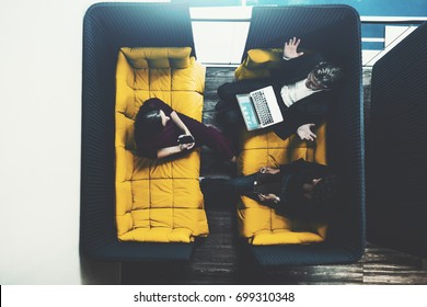 Small Fenced Soft Meeting Area In Chill Out Zone Of Office With Three Business Persons Having There Work Meeting Or Conversation During Coffee Break: Man With Laptop And Two Female Colleagues