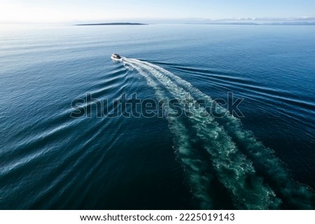 Small ferry boat in blue ocean on the way to Aran island, Ireland. Wake behind cruise ship. Warm sunny day with clear blue sky. Travel and transportation industry. Popular route from Doolin port.