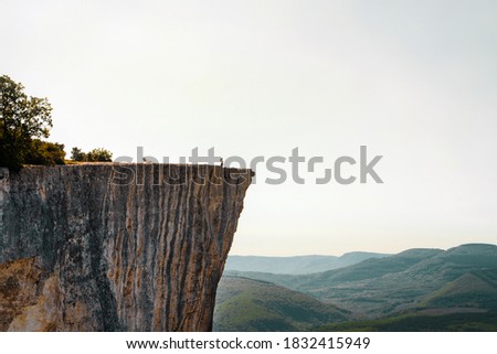 A small figure of a woman tourist standing on the edge of a cliff in the summer mountains. The concept of a small man in the midst of a powerful nature.