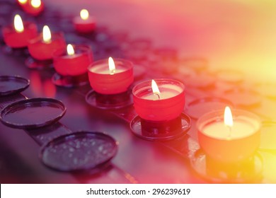 Small Firing Candles In Catholic Church On Dark Background. Filtered Photo With Effects