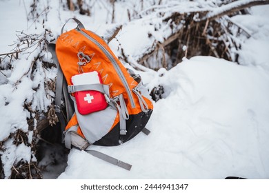 A small first aid kit is attached to the backpack, the orange backpack stands on the snow in the winter forest, camping equipment. High quality photo - Powered by Shutterstock