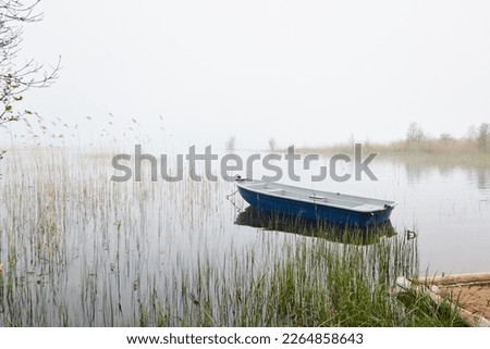 Small fishing boat anchored in a forest lake. Fog, rain. Reflections on water. Transportation, traditional craft, recreation, leisure activity, healthy lifestyle, local tourism theme. Spring landscape
