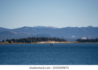 a small fishing boat in a dark blue water lake, forest and mountain backdrop - Powered by Shutterstock