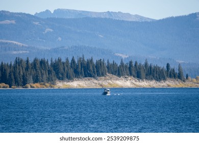 a small fishing boat in a dark blue water lake, forest and mountain backdrop - Powered by Shutterstock