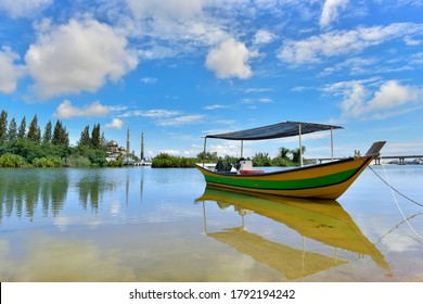 Small Fishing Boat Floats On The Terengganu River And The Crystal Mosque In A Background.