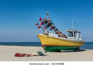 Small Fishing Boat In Reggae Colors On Baltic Beach Against Blue Sky.