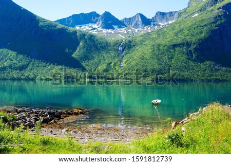 A small fjord with turquoise water, surrounded by mountains. The mountain river flows on a steep slope. Cycling tour in Polar Norway.