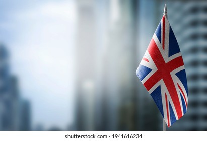 A Small Flag Of United Kingdom On The Background Of An Urban Abstract Blurred Background.