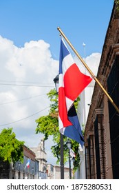 Small flagpole on a wall with a Dominican Republic flag hanging on a house wall outside. The flag is waving in the gentle wind. It is a beautiful sunny summer day