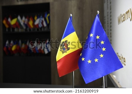 Small flags of Republic of Moldova and European Union on flagpole in foreground with multiple other small flags in background. Concept of EU perspective for Modova. 
