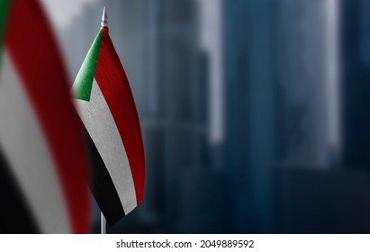 Small Flags Of Sudan On A Blurry Background Of The City