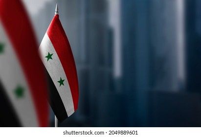 Small Flags Of Syria On A Blurry Background Of The City