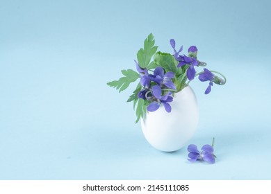 Small Flower Arrangement. Eggshell With Violets On A Blue Background. Easter Decor And Copy Space.