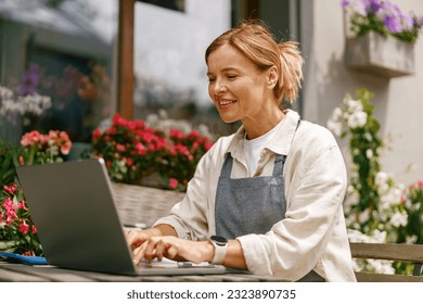 Small flower shop owner florist wearing apron working on laptop and taking online orders in store  - Powered by Shutterstock