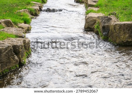Small flowing stream bordered by natural stones and green grass in a landscaped park with moving water and peaceful outdoor scenery