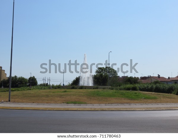 A small fountain in the middle of a roundabout\
dividing the sea from the hill an embellishment to improve the view\
/ landscape