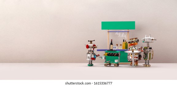 A Small Funny Robot Waiter Carries A Cart With Alcohol, Wine Bottles And Dishes For Two Guests Of Robots Who Celebrate The System Update. Bar Counter Background. Copy Space