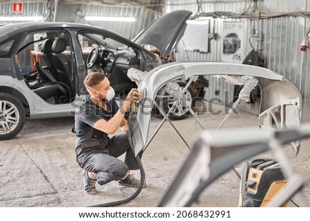 Small Garage. The mechanic works with a grinding tool. Sanding of car elements. Painting car service. Repairing car section after the accident.