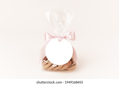 Small gift with cookies in a plastic bag tied up to a bow with a pink ribbon and a round white gift tag attached - Shutterstock ID 1949168455