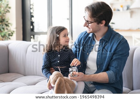 Small girl daughter and her young father putting money to the moneybox piggy bank. Personal Savings. Saving money concept. For future, mortgage loan savings home in crisis coronavirus concept.