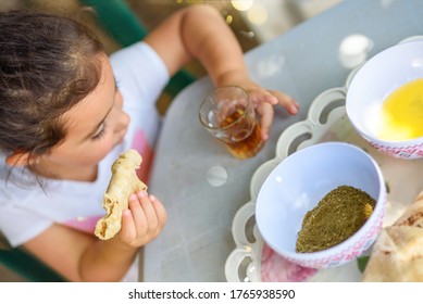 A Small Girl Drinking Tea And Eating Flatbread With Olive Oil And Zaatar At Home. Little Kid Enjoy The Food And Drink And Have Great Fun Outdoors In Backyard At Sunny Day.