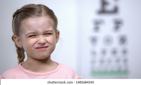 Small Girl Frowning, Trying To See Letter On Vision Testing Table Blurred Vision