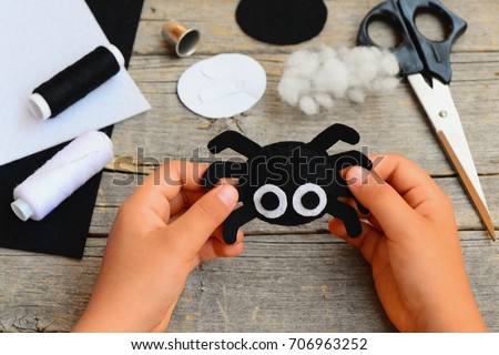 Small girl holds a felt spider ornament in his hand. Girl made a Halloween felt spider crafts. Easy felt crafts for beginners. Halloween sewing craft kit