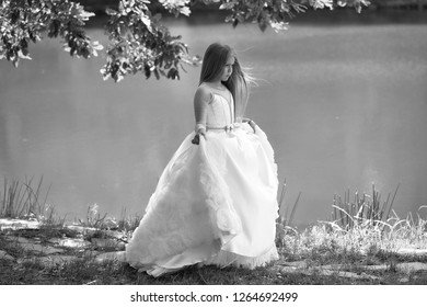 Small Girl Kid With Long Blonde Hair And Pretty Smiling Happy Face In Prom Princess White Dress Standing Sunny Day Outdoor Near Water