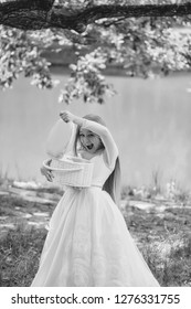 Small Girl Kid With Long Blonde Hair And Pretty Smiling Happy Face In Prom Princess White Dress Standing Sunny Day Outdoor Near Water With Basket