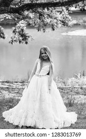 Small Girl Kid With Long Blonde Hair And Pretty Smiling Happy Face In Prom Princess White Dress Standing Sunny Day Outdoor Near Water