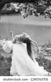 Small Girl Kid With Long Blonde Hair And Pretty Smiling Happy Face In Prom Princess White Dress Standing Sunny Day Outdoor Near Water With Basket