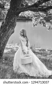 Small Girl Kid With Long Blonde Hair And Pretty Smiling Happy Face In Prom Princess White Dress Standing Sunny Day Outdoor Near Water With Basket