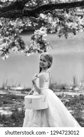 Small Girl Kid With Long Blonde Hair And Pretty Smiling Happy Face In Prom Princess White Dress Standing Sunny Day Outdoor Near Water With Basket