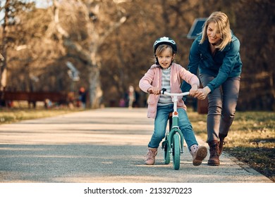 Small Girl Learning To Ride Bicycle With Help Of Her Mother In The Park. Copy Space.