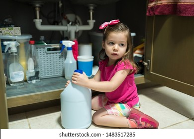 Small Girl Looking Away While Sitting With Container By Open Cabinet In Kitchen At Home