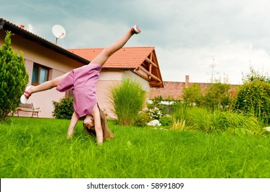 Small girl making cartwheel on garden with family house in background