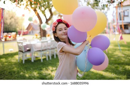 Small girl outdoors in garden in summer, playing with balloons.