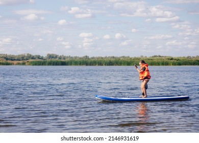 Small girl paddle boarding by herself on lake with oar in hands in orange life jacket. Active holidays full of adventures. Inculcation of love for sports from childhood. - Shutterstock ID 2146931619