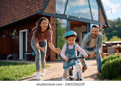 Small girl riding bicycle while her parents are assisting her outdoors.  - Powered by Shutterstock