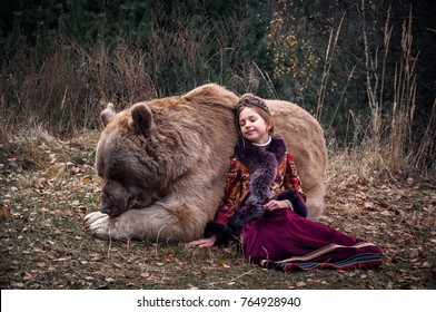 A small girl in the russian traditional costume walking with a real big brown bear in the forest. Late autumn period 