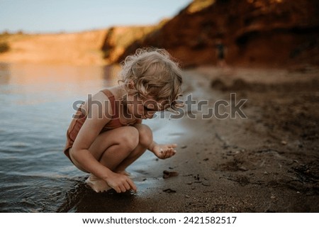 Small girl in swimsuit playing at beach, crouching, seraching for shells in the sand.