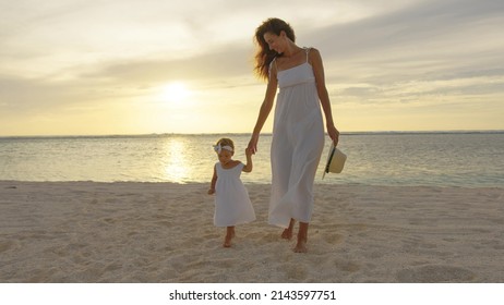 Small girl walking with mother at tropical beach Sunset in the background