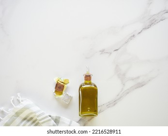 Small Glass Bottle With Olive Oil, Unwrapped Stock Cube And Tea Towel On White Marble Kitchen Counter, Top View With Copy Space.