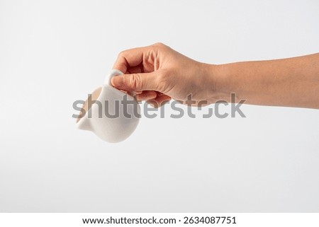 Small glass bottle with a pouring pattern. The glass bottle is a cloudy white color with a hand holding it on white background.