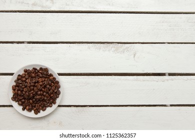 Small Glass Plate With Coffee Beans On White Table, Top View, Left Down Corner, Empty Copy Space