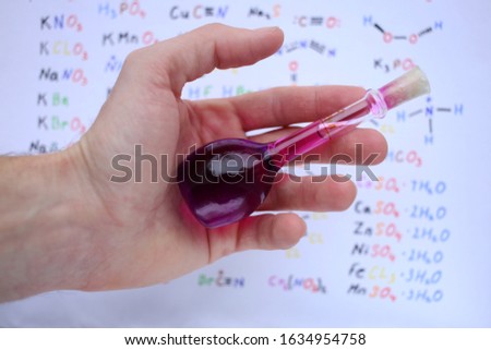 Small glass pycnometer for measuring the density of liquid substances, with purple liquid in the palm of a hand.